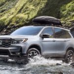 A silver 2022 Honda Passport TrailSport is shown driving through a river.