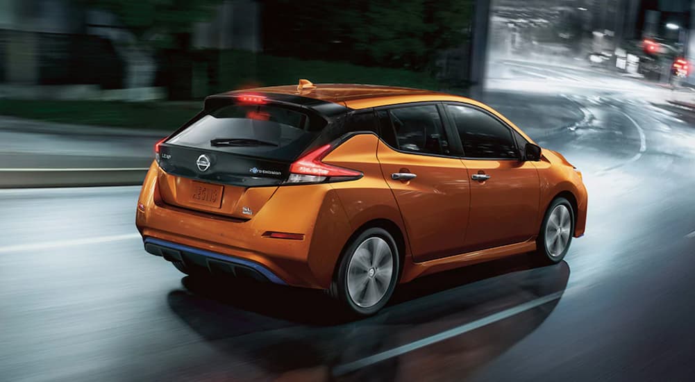 An orange 2022 Nissan LEAF is shown from the rear while rounding a corner.