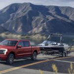 A red 2022 Ford F-150 Lightning is shown towing a boat on an open road after leaving a Ford Lightning dealer.