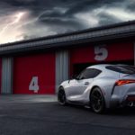 A silver 2022 Toyota GR Supra is shown from the rear while parked in the pits of a racetrack.