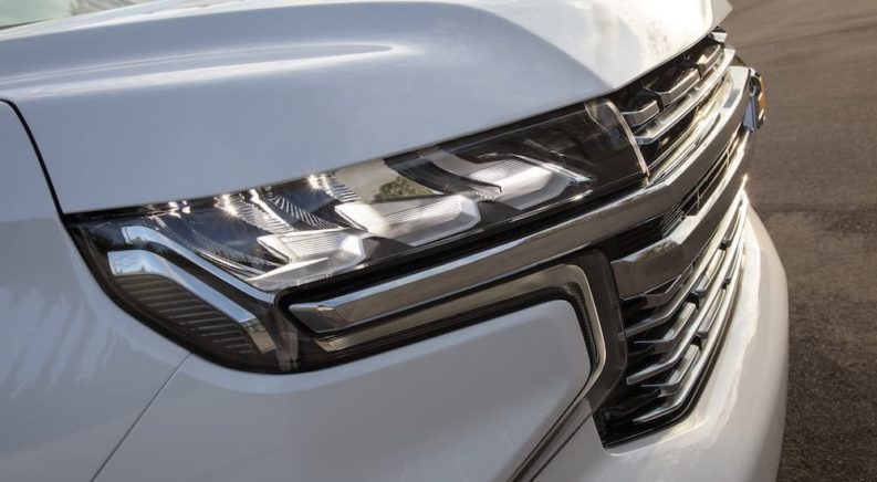 A close up shows the passenger side headlight on one of the most popular vehicle at used car dealers, a white 2021 Chevy Suburban.