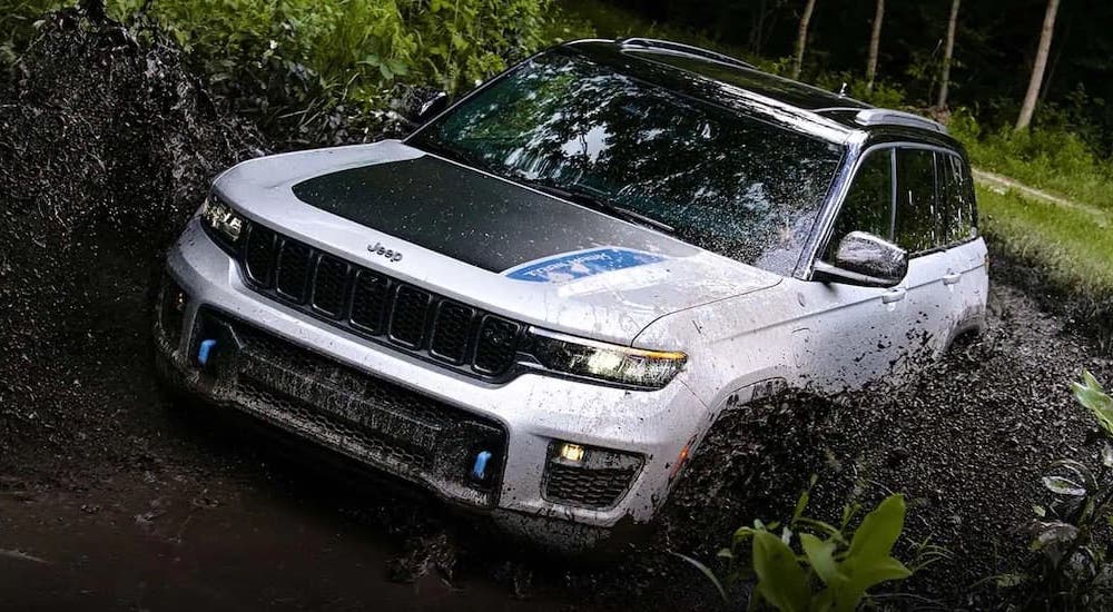 A white 2022 Jeep Grand Cherokee 4xe is shown from the front at an angle while it drives through mud.