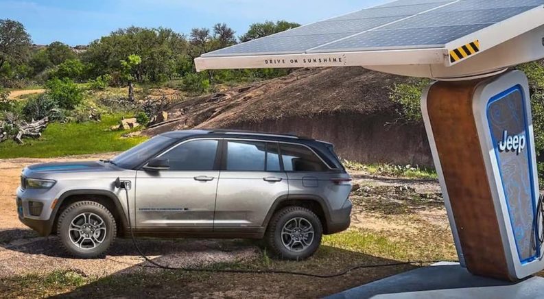 A silver 2022 Jeep Grand Cherokee 4xe is shown at a charging station in the wilderness.