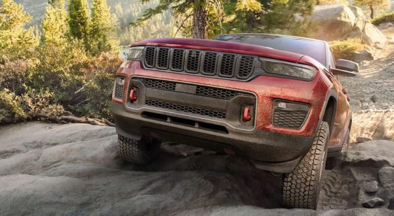 A red 2022 Jeep Grand Cherokee Trailhawk is shown from the front while climbing over a rock.