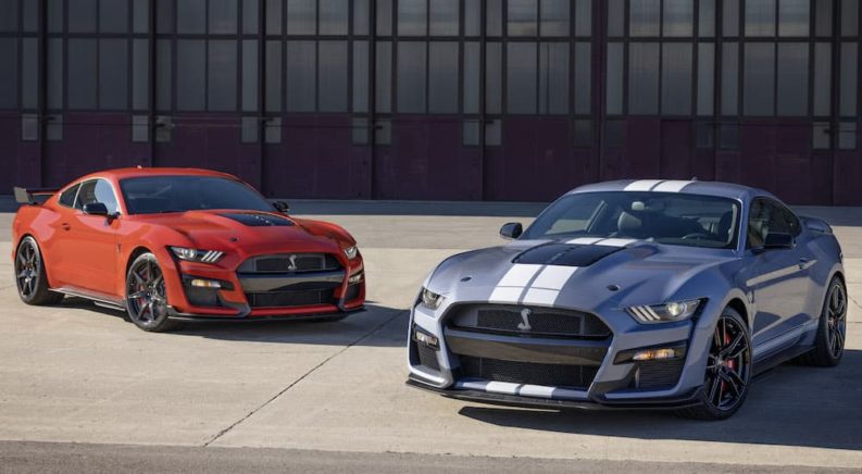 A red 2022 Ford Mustang GT500 and blue Heritage Edition are shown angled toward each other in an empty lot.