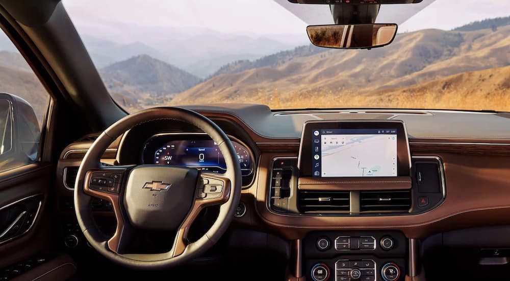 The tan interior of a 2023 Chevy Suburban shows the steering wheel and infotainment screen.