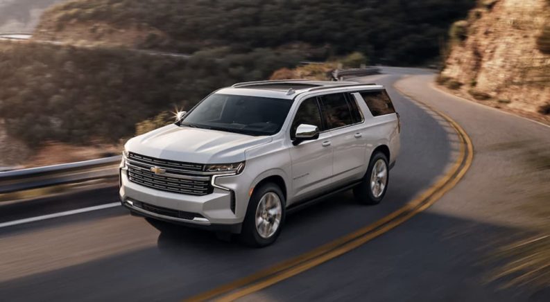 A white 2023 Chevy Suburban is shown from the front driving on an open road.