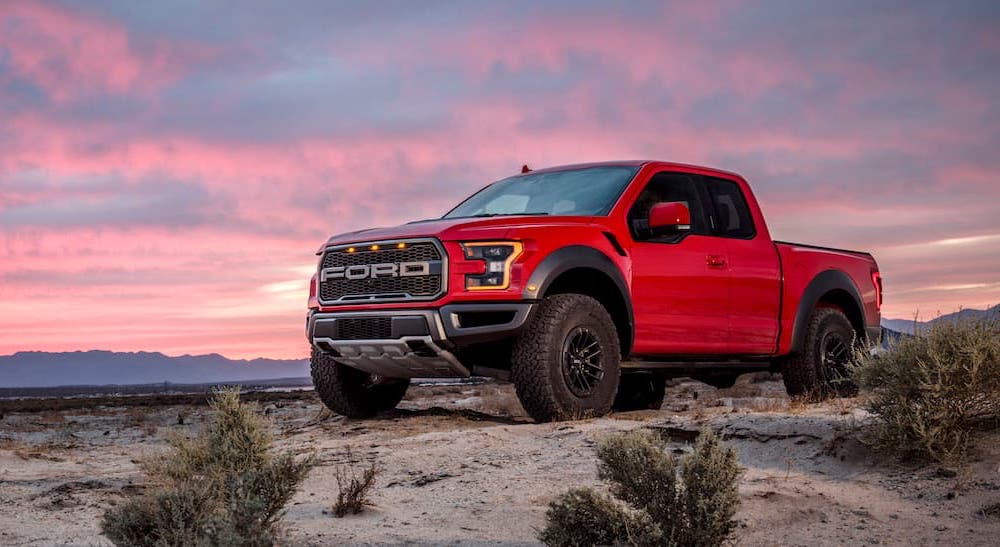 A red 2021 Ford F-150 Raptor is shown at sunset.