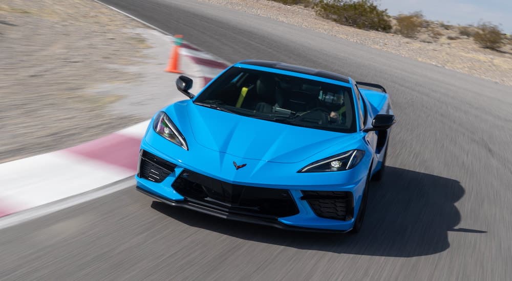 A blue 2023 Chevy Corvette is shown from the front driving on a racetrack.