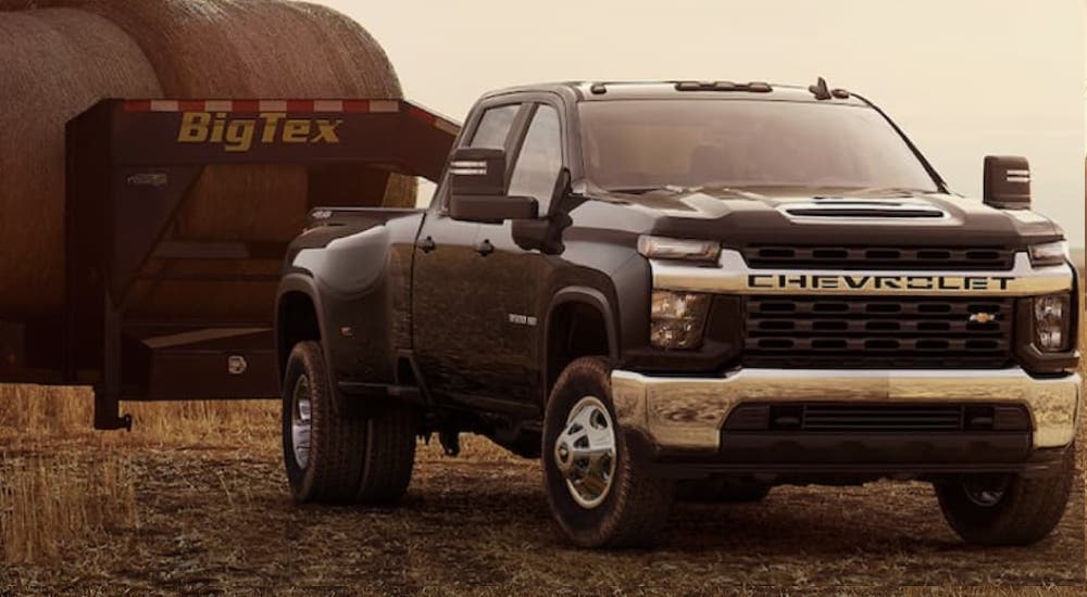 A black 2022 Chevy Silverado 3500HD is shown towing a trailer full of haybales.
