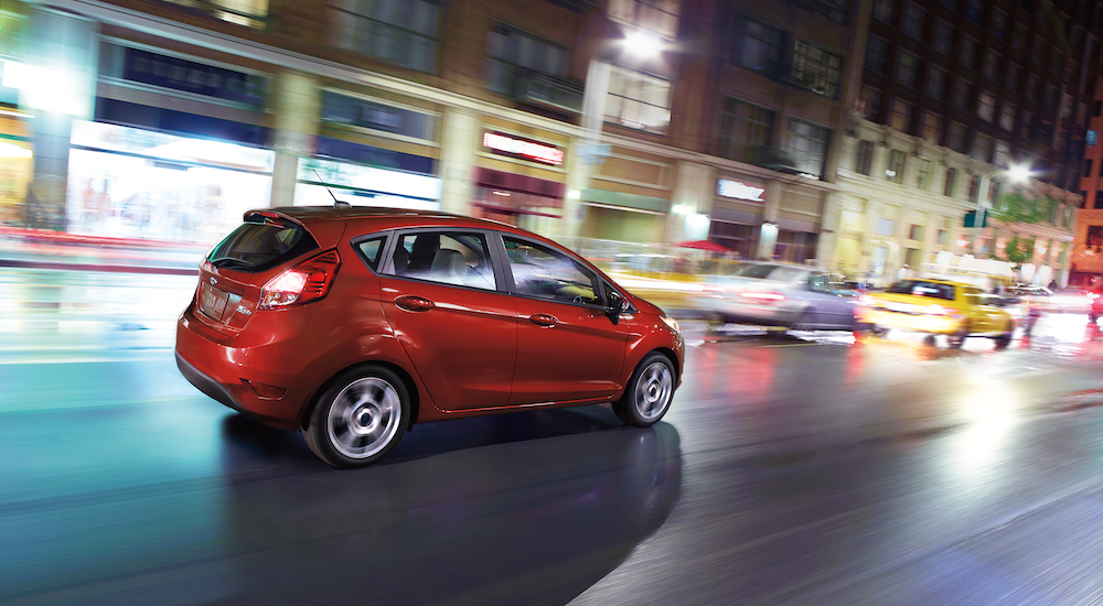 A red 2018 Ford Fiesta is shown driving through a city towards a Ford dealership near you.