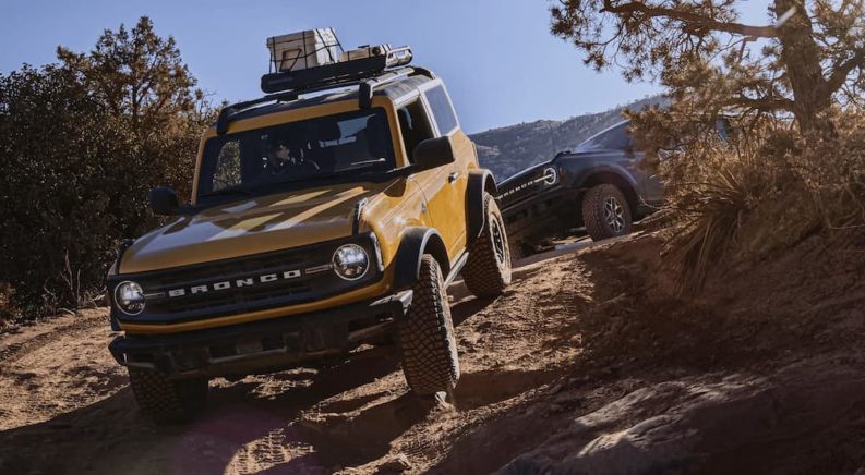 A yellow 2022 Ford Bronco is shown off-roading on a steep trail after viewing used SUVs Near Chapel Hill.
