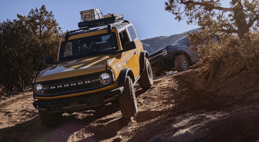 A yellow 2022 Ford Bronco is shown off-roading on a steep trail.