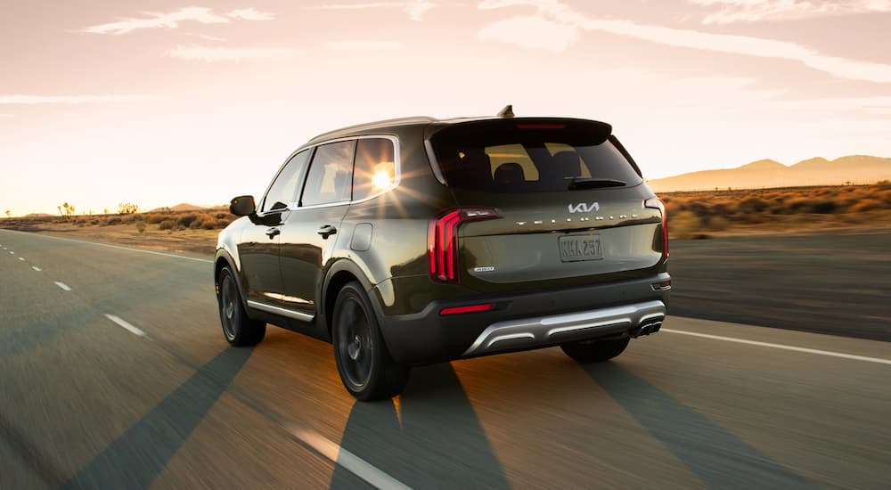 A green 2022 Kia Telluride is shown from the rear driving on an open road on a sunny day.