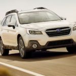 A white 2019 Subaru Outback is shown from a front angle while it drives down the road after leaving a used Subaru Outback dealership.