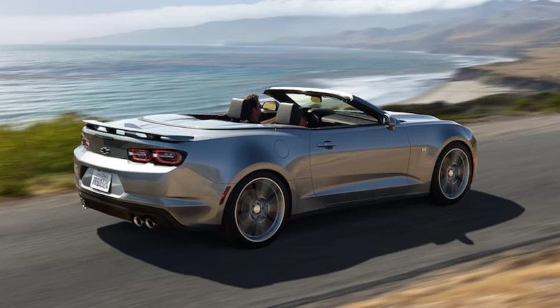 A silver 2021 Chevy Camaro Convertible is shown from the rear at an angle on a coastal road.
