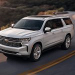 A white 2023 Chevy Suburban is shown from the front at an angle while driving down the road.