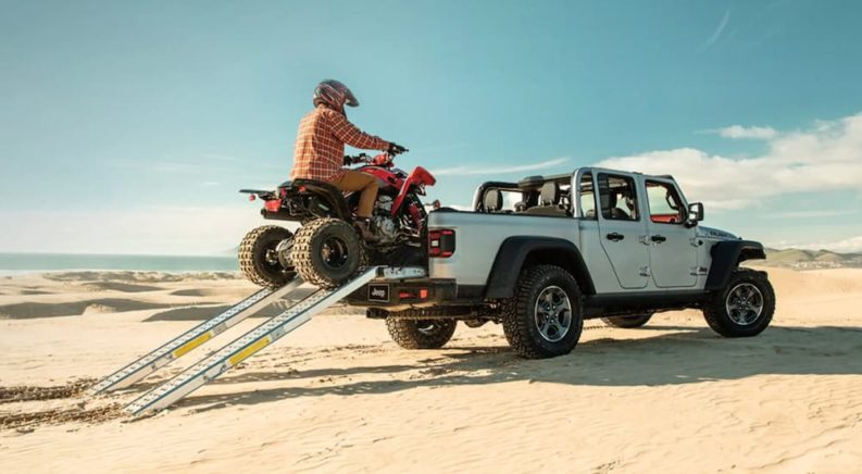 A silver 2022 Jeep Gladiator is shown from the rear while being loaded with a quad.