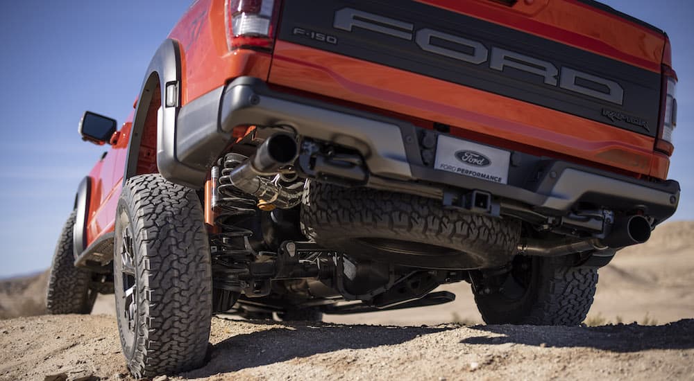 An orange 2022 Ford F-150 Raptor is shown from the rear at a low angle while traversing rocky terrain.