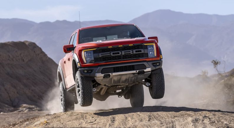 A red 2022 Ford F-150 Raptor is shown from the front while jumping over a hill.