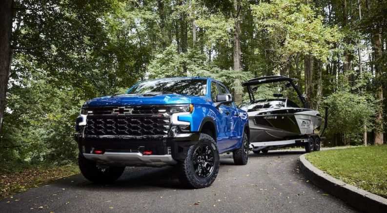 A blue 2022 Chevy Silverado 1500 ZR2 is shown towing a boat in a driveway.
