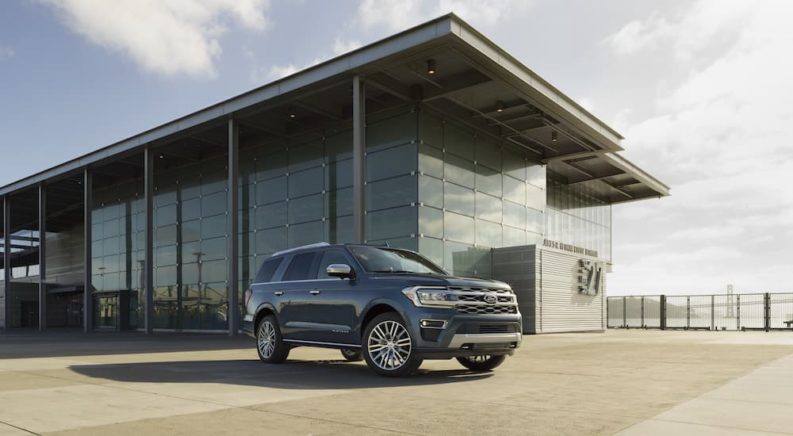 A blue 2022 Ford Expedition Platinum is shown from the front at an angle while parked in front of a glass building after the owner searched for 'Ford SUVs'.