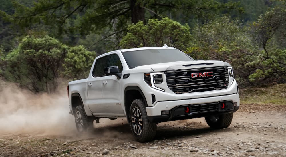 A white 2022 GMC Sierra 1500 AT4 is shown driving on a dusty dirt trail.