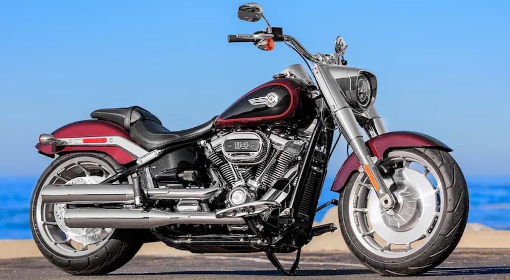 A red 2022 Harley-Davidson Fat Boy 114 is shown from the side while parked on the beach.
