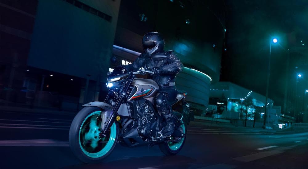 A grey 2022 Yamaha MT09 is shown from the front at an angle while driving down a city street at night.