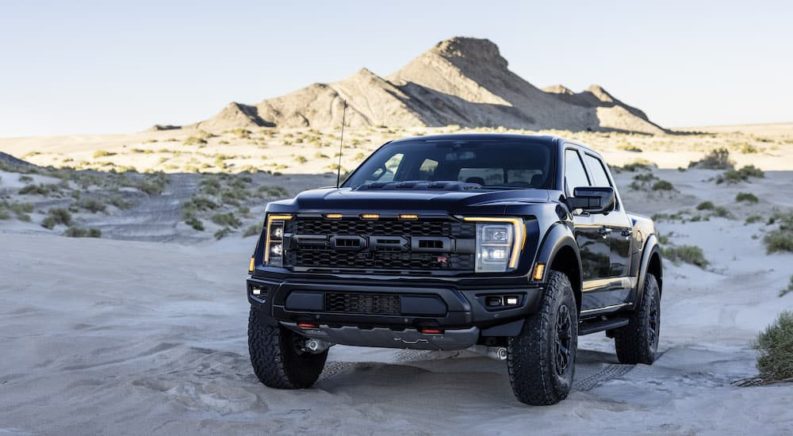 A dark blue 2023 Ford F-150 Raptor R is shown from the front at an angle while driving in a desert.