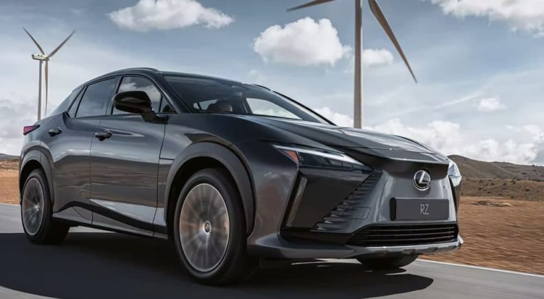 A grey 2023 Lexus RZ is shown from the side driving past windmills.