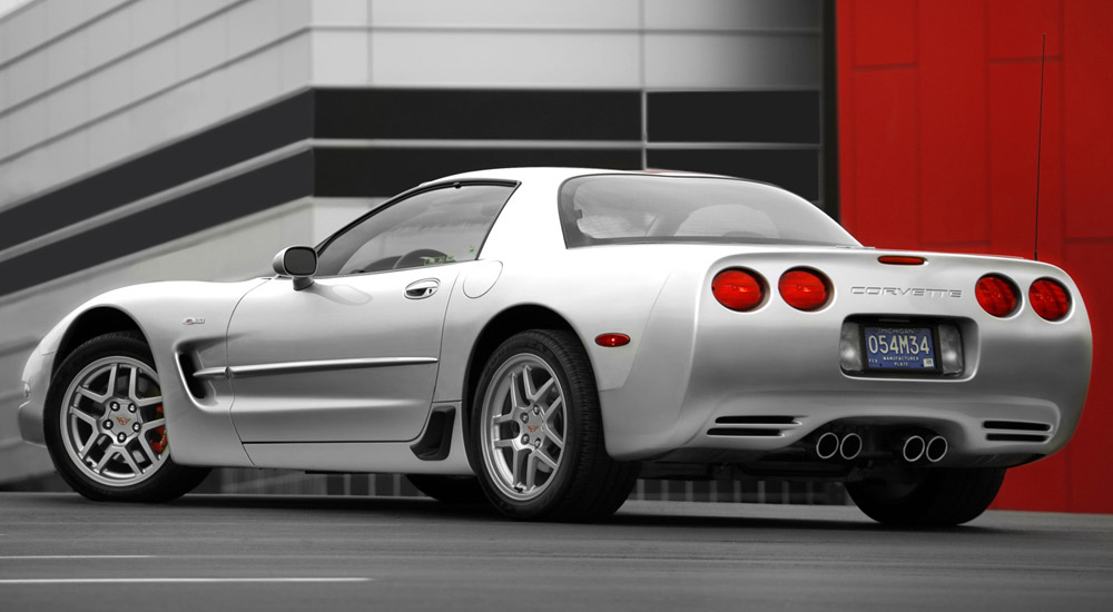 A silver 2003 Chevy Corvette is shown parked outside of a city building.