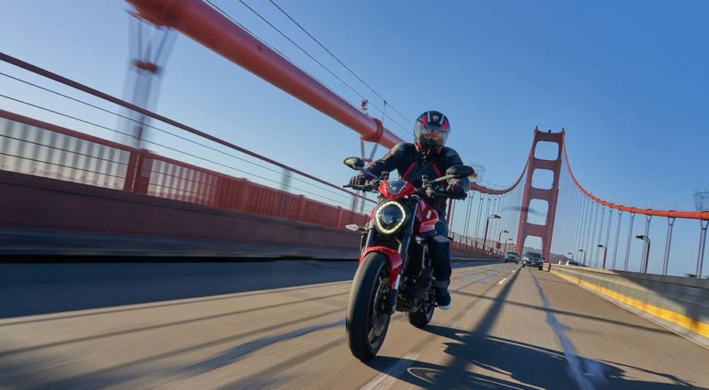 A red 2022 Ducati Monster Plus is shown from the front while driving over a bridge.
