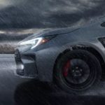 A close-up of the wheel of a grey 2023 Toyota GR Corolla is shown in the rain.