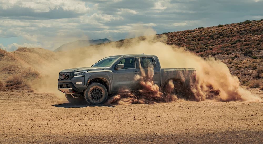 A grey 2022 Nissan Frontier is shown from the side while kicking up dust off-road.