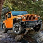 An orange 2022 Jeep Wrangler is shown from the front while driving over a rock.
