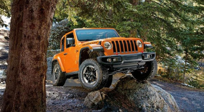 An orange 2022 Jeep Wrangler is shown from the front while driving over a rock.