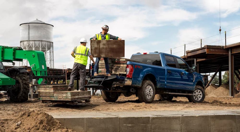 A blue 2022 Ford F-250 is shown from the rear while being loaded on a jobsite.