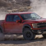 A red 2022 Ford F-150 Raptor is shown from the front at an angle while driving off-road.