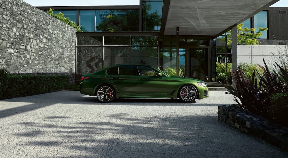 A green 2021 BMW M550i is shown from the side while parked in a driveway.