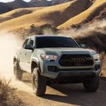 A grey 2023 Toyota Tacoma is shown from the front at an angle while driving down a dirt trail.