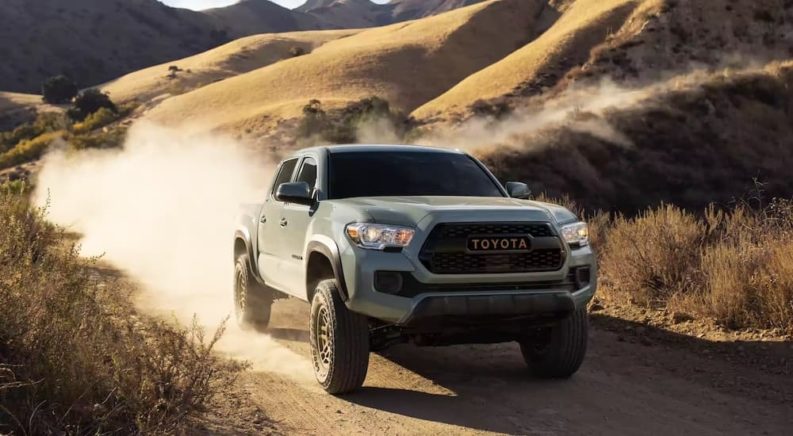 A grey 2023 Toyota Tacoma is shown from the front at an angle while driving down a dirt trail.