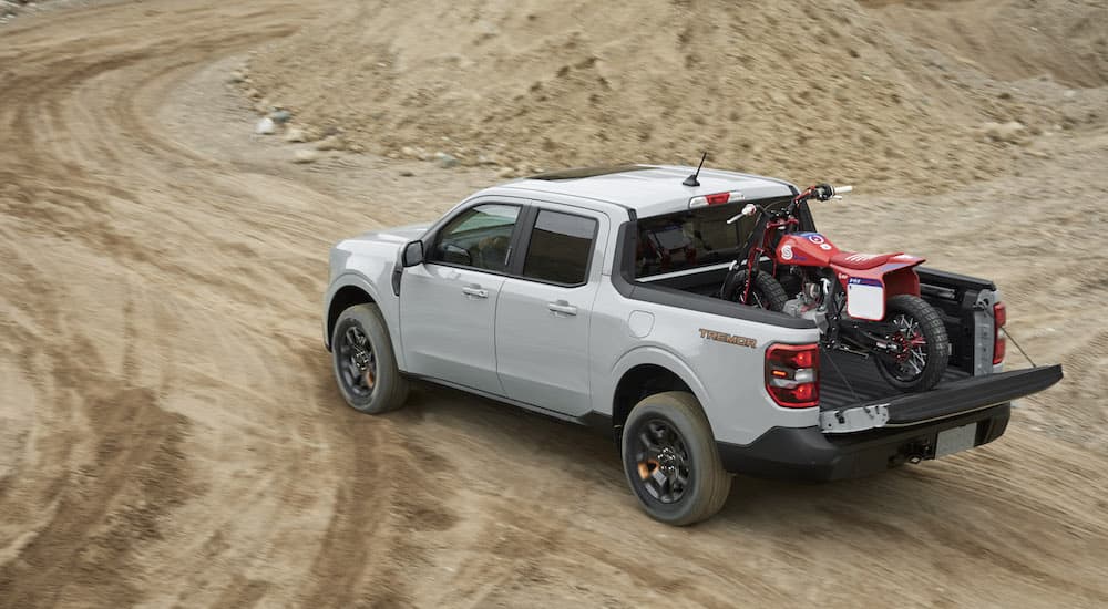 A grey 2022 Ford Maverick Tremor is shown from the rear at an angle while hauling a dirt bike off-road.