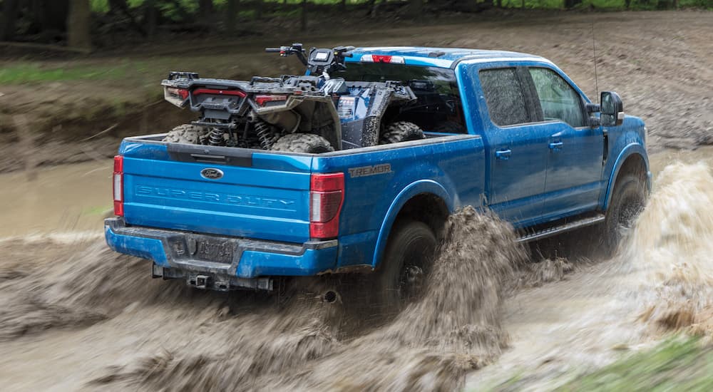 A blue 2022 Ford F-250 Tremor is shown from the rear while hauling an ATV through mud.