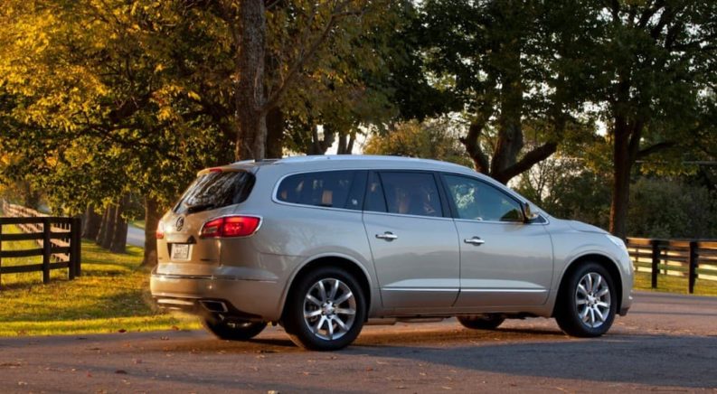 A popular Buick SUV, a tan 2014 Buick Enclave, is shown from the side parked in front of trees.