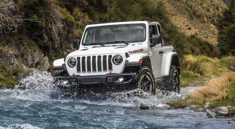 A white 2021 Jeep Wrangler Rubicon is shown driving through a river.