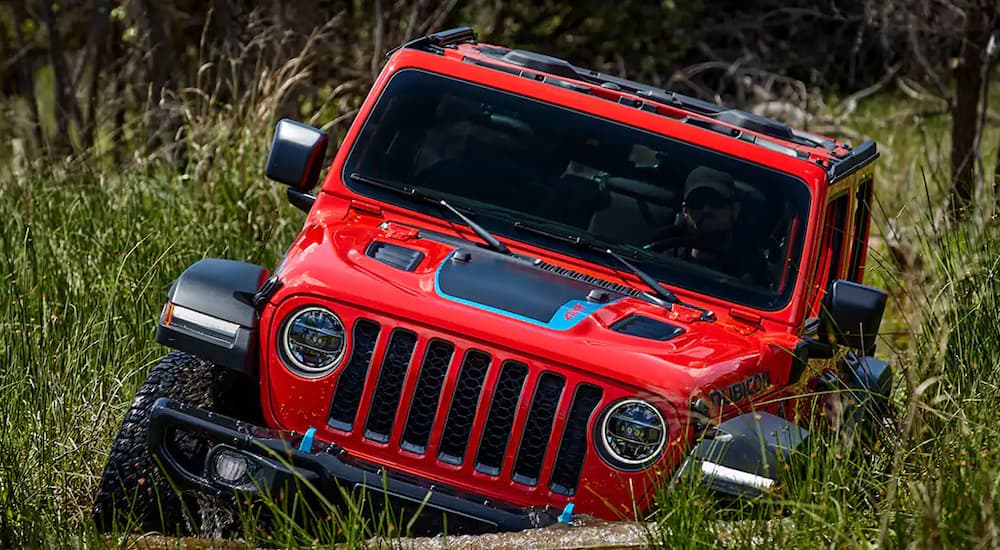 A red 2022 Jeep Wrangler 4xe Unlimited Rubicon is shown off-roading through tall grass.