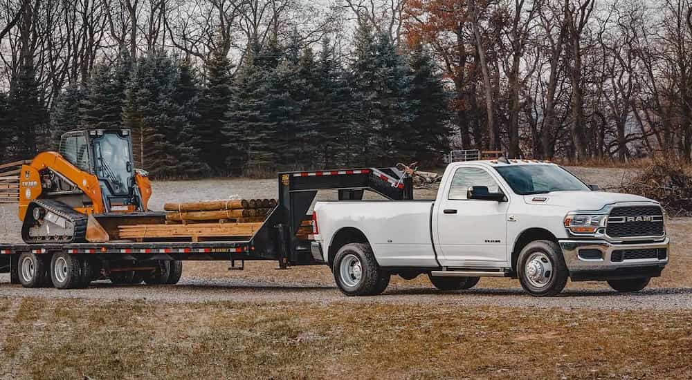 A white 2022 Ram 3500 Dually is shown from the front at an angle while towing a loader.
