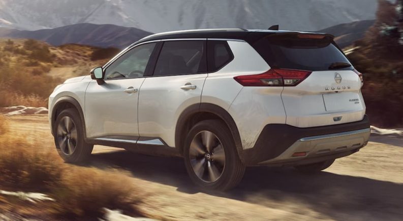 A white 2023 Nissan Rogue is shown driving on a dirt road.