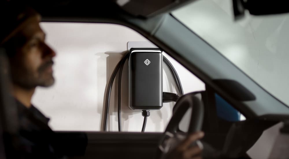 A man is shown sitting in a Rivian R1S next to an EV wall charging unit.